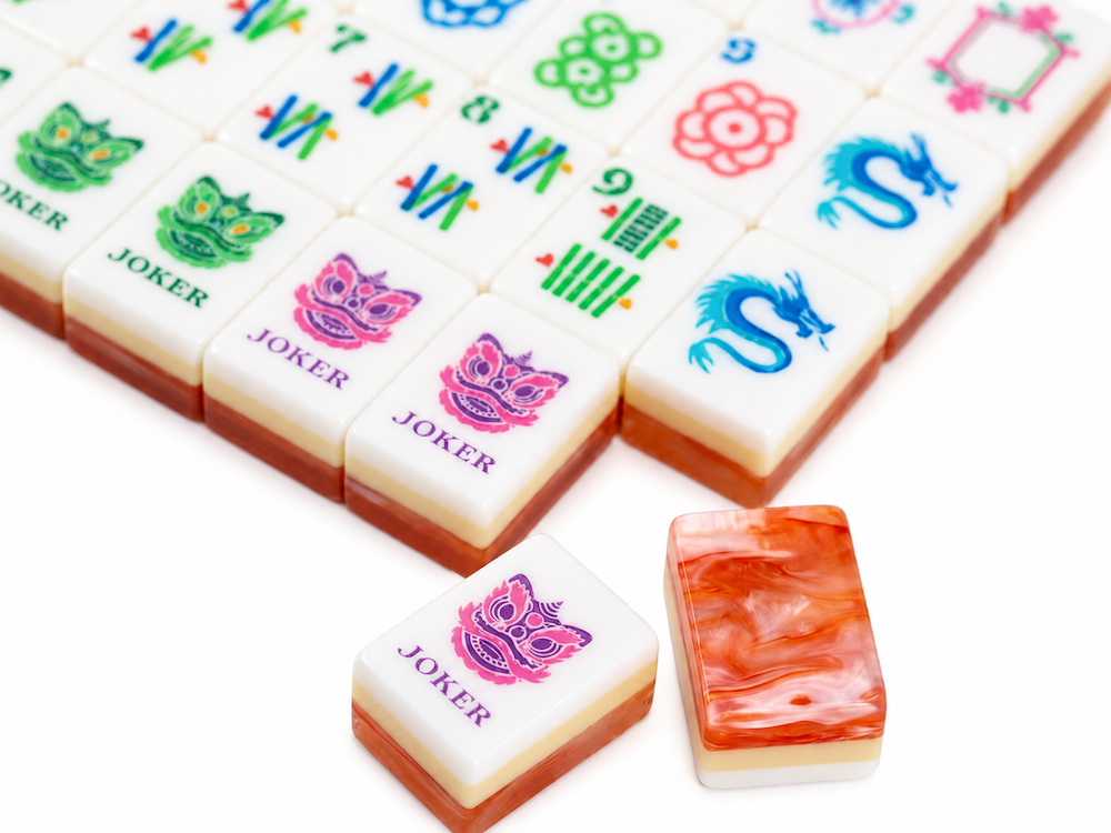 Close-up of mahjong tiles with pink and orange tiles, plus joker symbols and coral backs