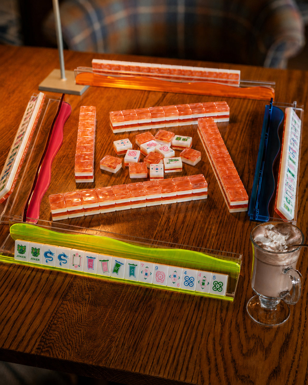 Mahjong tile rack with coral-orange tiles and small game pieces on wooden table