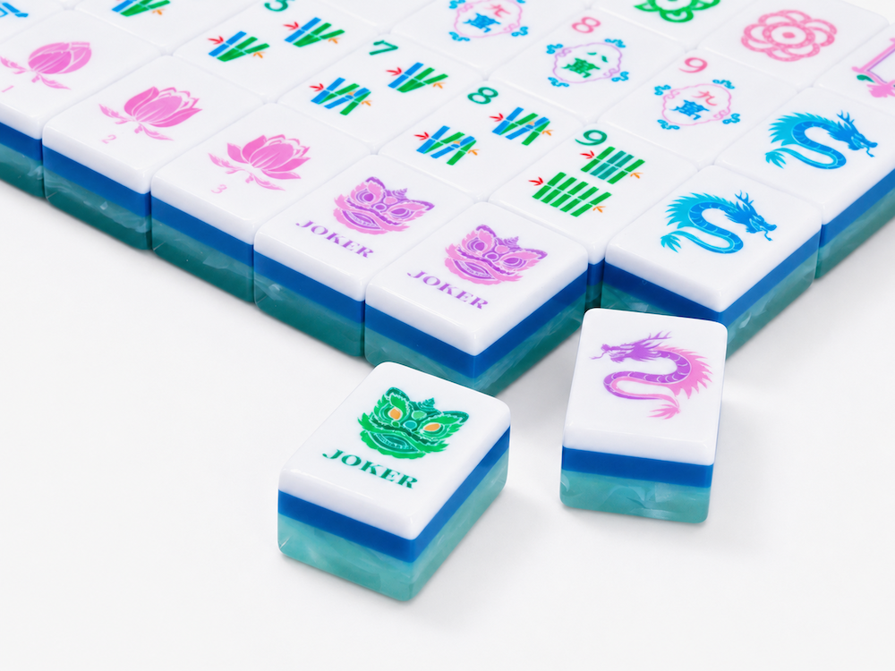 Mahjong tiles on white surface with flower and blue dragon joker symbols and loose joker tile
